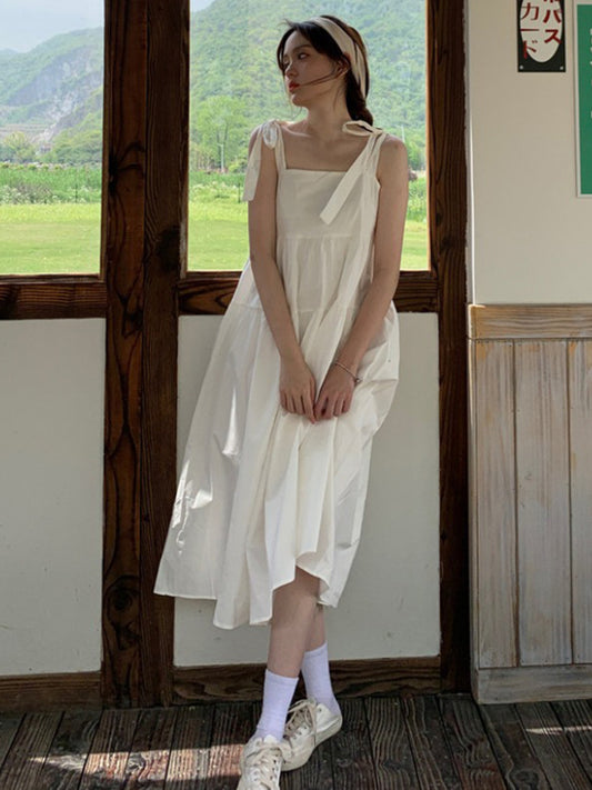 Woman in a white dress standing in a room with large windows showing a green landscape.