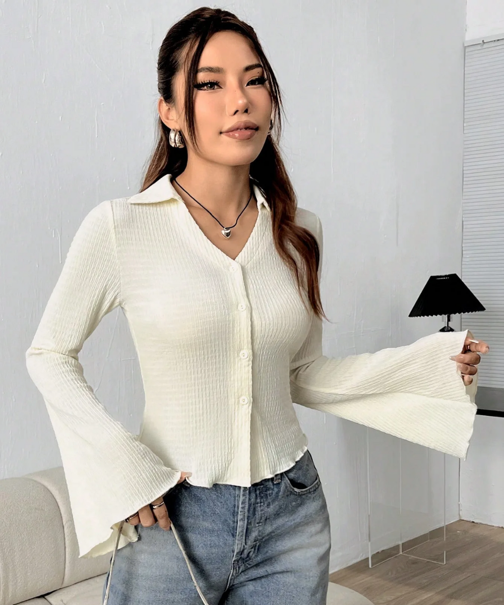 Woman wearing a white ribbed blouse and blue jeans indoors.