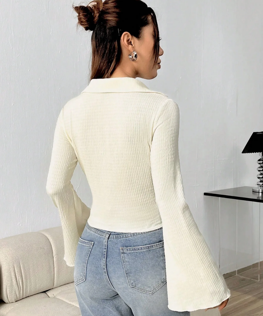 Woman wearing a white ribbed sweater with bell sleeves in a minimal indoor setting.