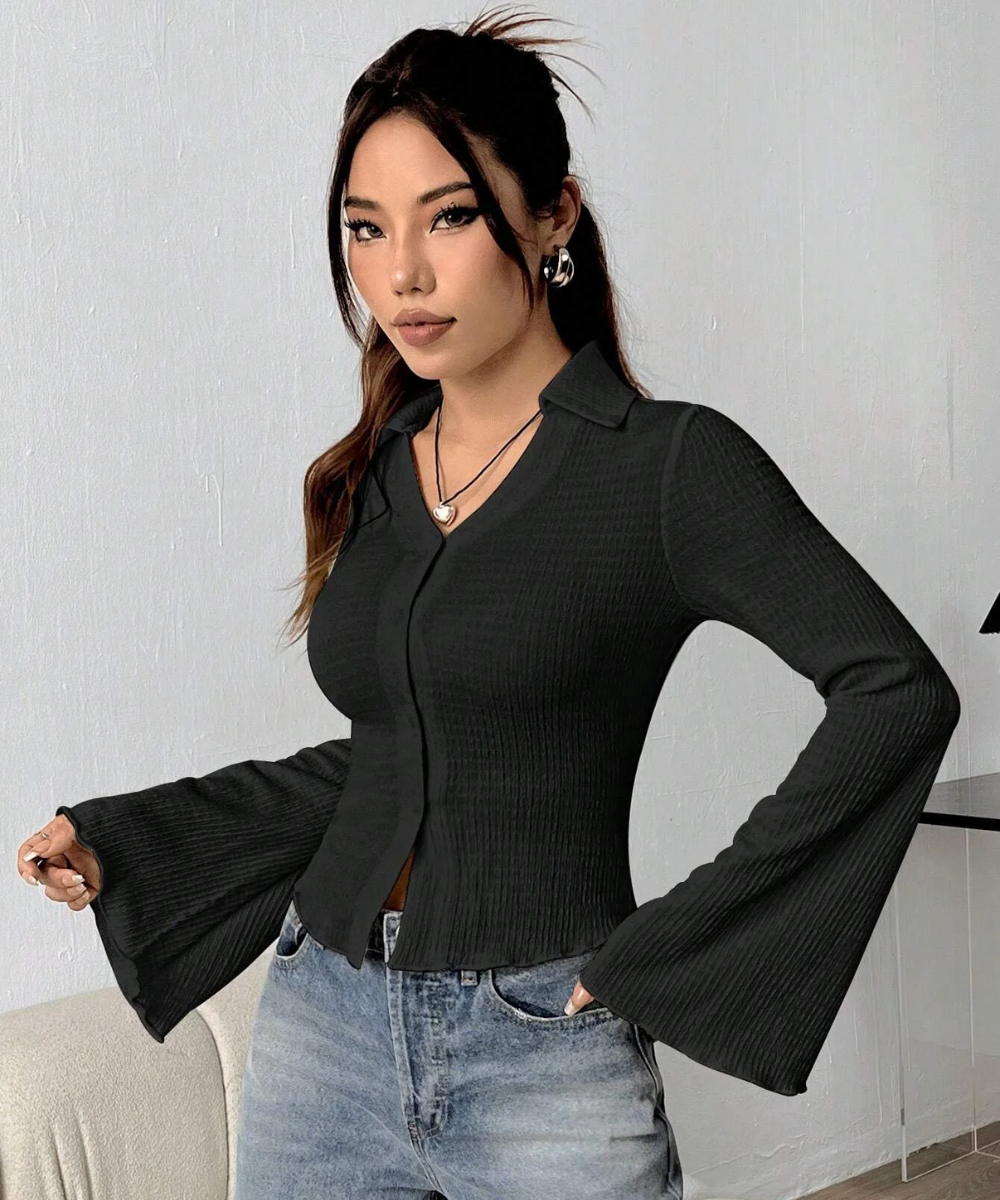 Woman wearing a black ribbed blouse with bell sleeves against a white wall.
