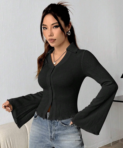 Woman wearing a black ribbed blouse with bell sleeves against a white wall.