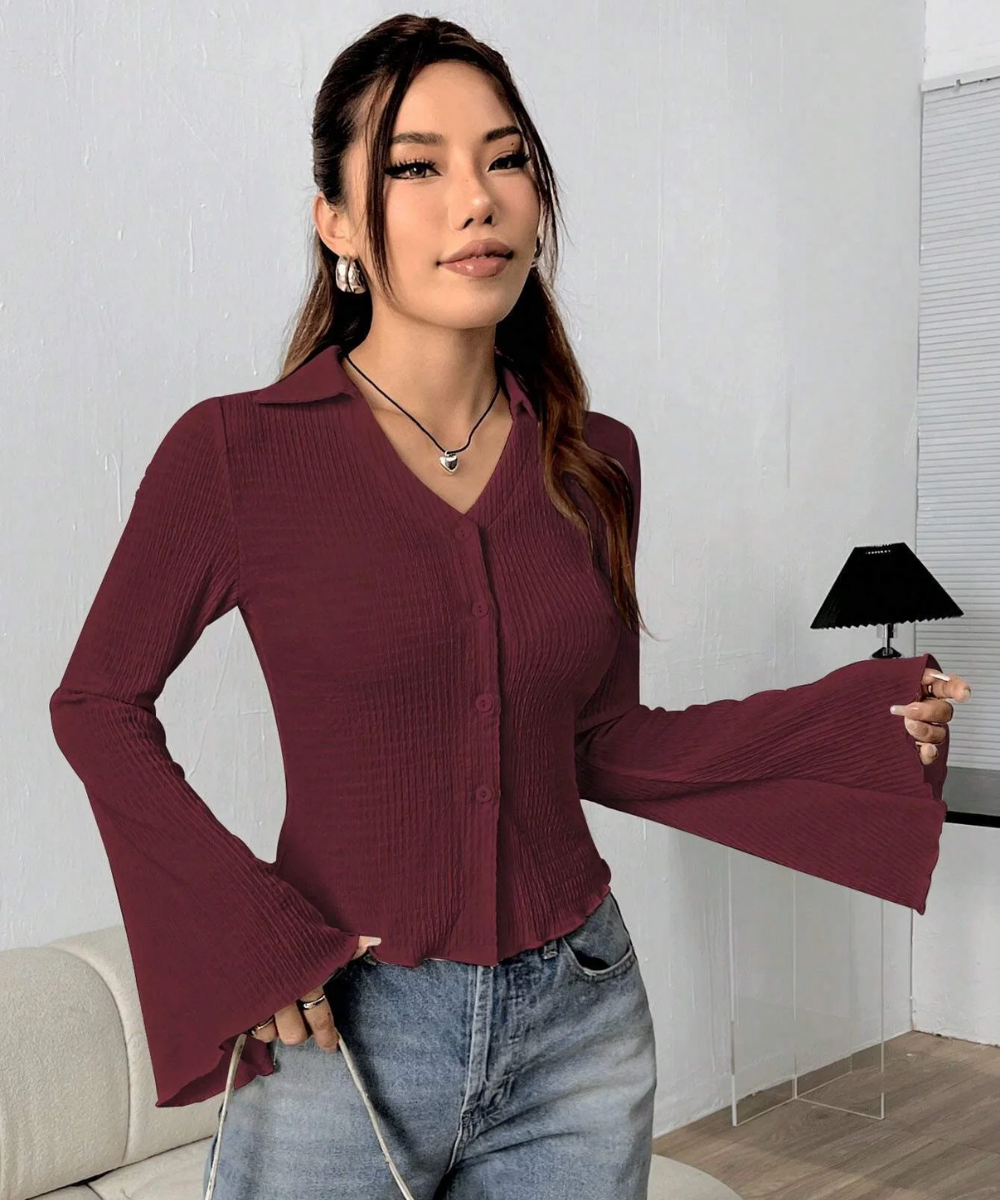 Woman wearing a burgundy ribbed blouse and jeans indoors.