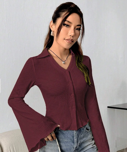 Woman wearing a maroon ribbed blouse and blue jeans against a white wall.